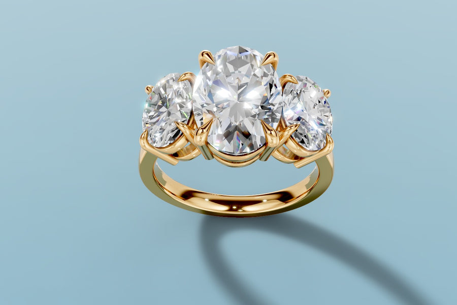 Three-stone oval lab diamond ring with a larger oval center and two smaller oval side stones in four-claw prong settings on a plain polished shank in 14k yellow gold, three-quarter view