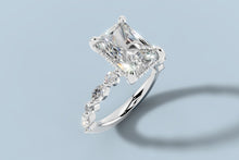Load image into Gallery viewer, Angled close view of radiant lab diamond engagement ring with hidden halo and round and marquise accent band in 14k white gold
