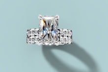 Load image into Gallery viewer, Top view of radiant diamond double-band ring showing the four claw prongs and two rows of round diamonds in 14k white gold
