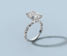 Load image into Gallery viewer, Radiant diamond ring standing upright showing the four-prong setting, hidden halo and marquise-and-round band in 14k white gold
